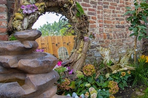 A stone archway with a wooden door, surrounded by a garden with various plants and flowers.