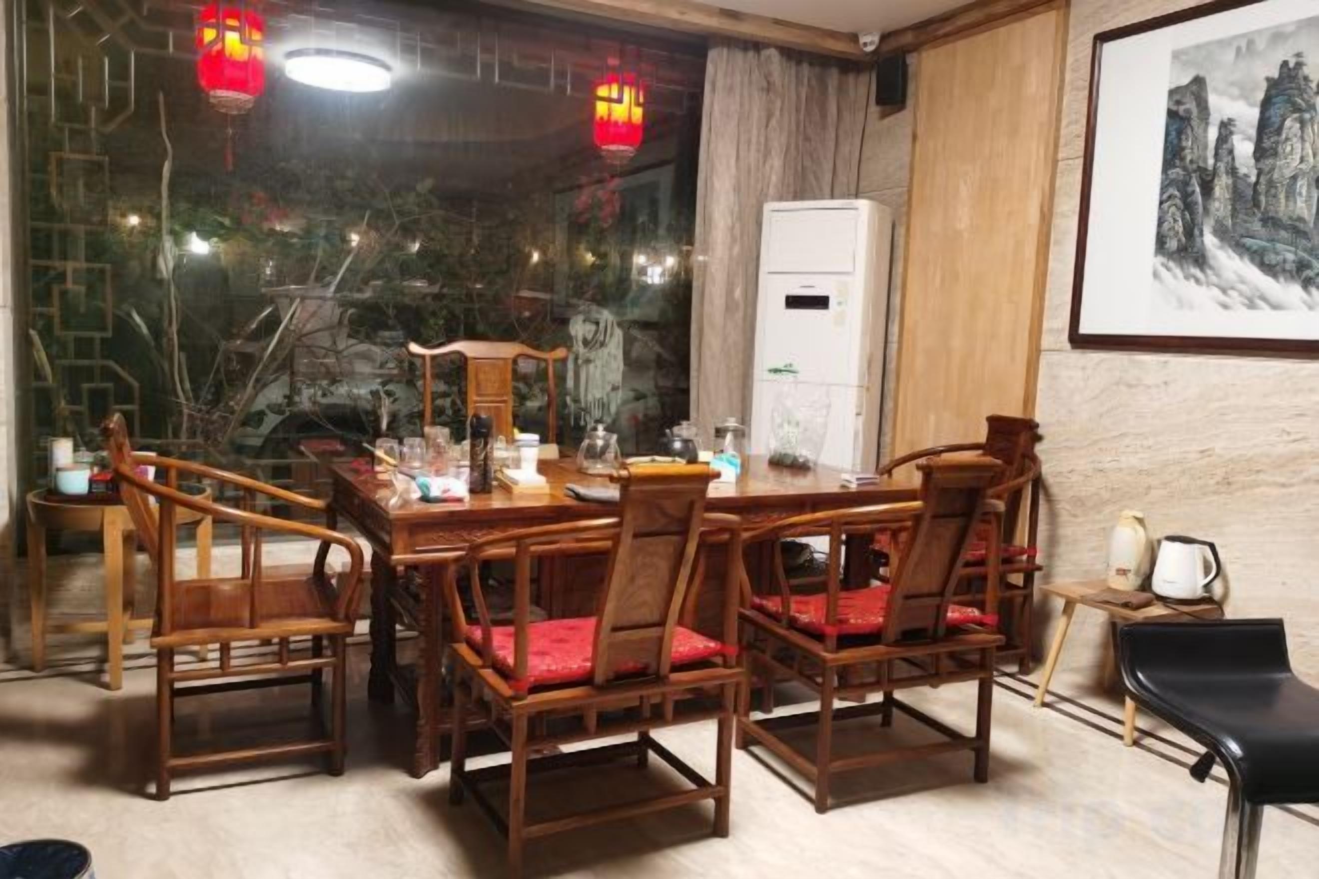 A dining area with a wooden table and chairs, a refrigerator, and a framed artwork on the wall.