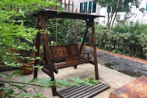 Um conjunto de balanço de madeira em área de jardim com parede de tijolos e plantas em vasos.