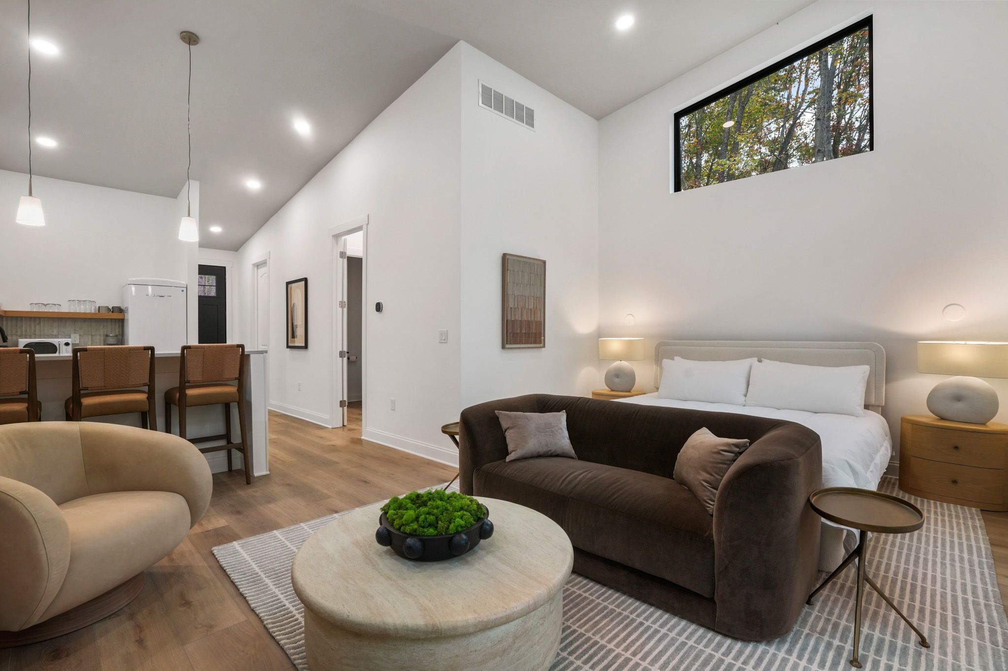 A modern living room with a sofa, a round coffee table with a plant, and a bed with a nightstand.