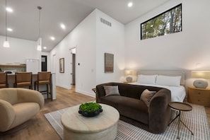 Ein modernes Wohnzimmer mit einer Couch, einem runden Couchtisch mit einer Pflanze und einem Bett mit einem Nachttisch.