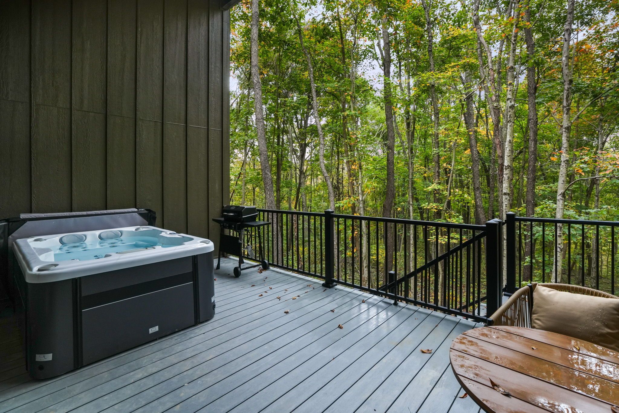A hot tub on a wooden deck with a view of a forest.