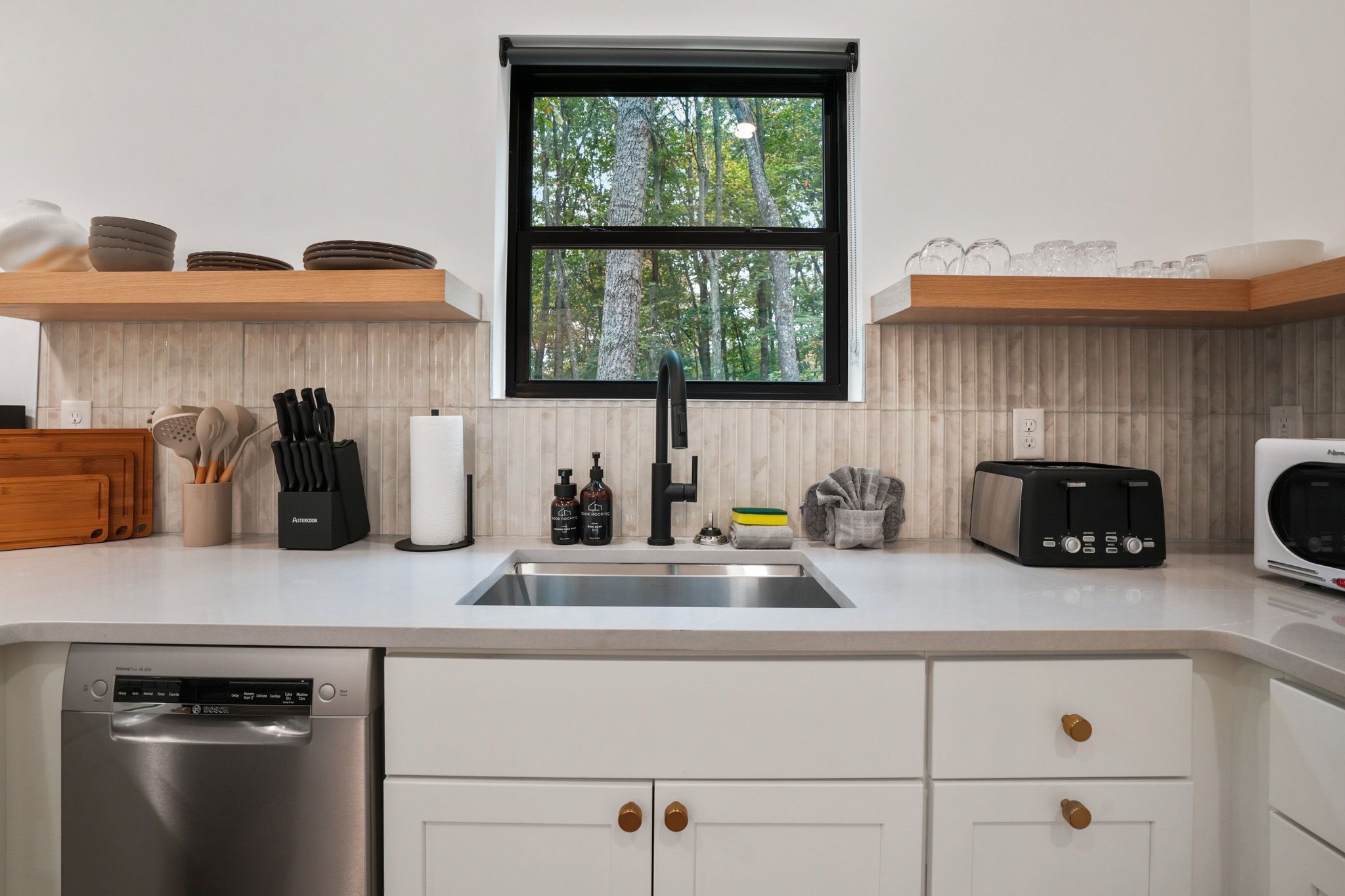 A modern kitchen with a stainless steel dishwasher, a black Bosch toaster, and a window with a view of trees.