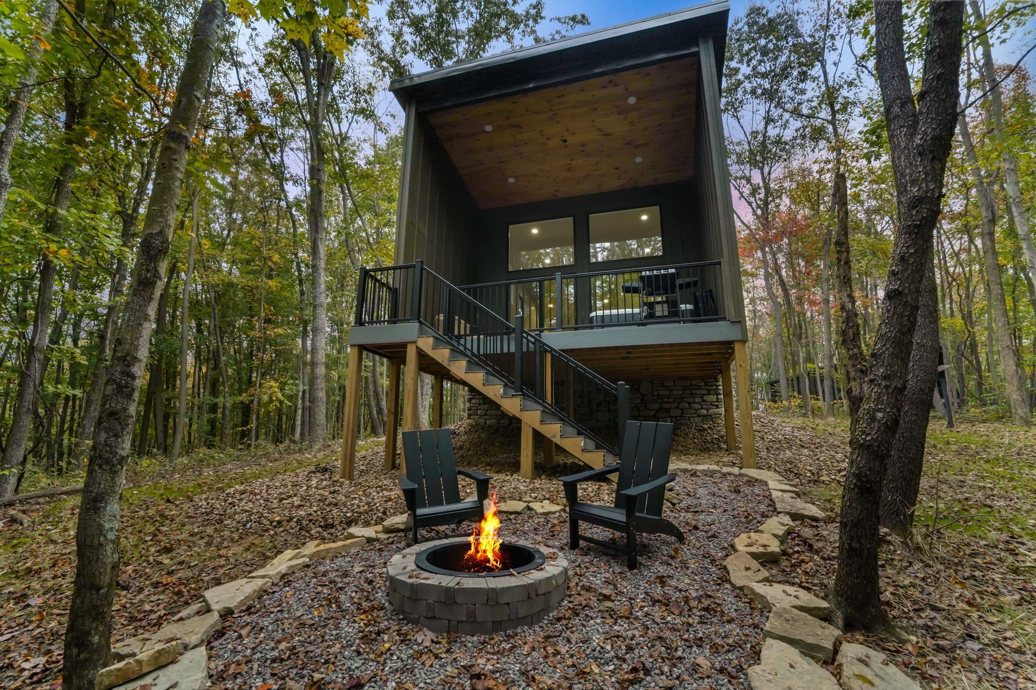 Una cabaña con chimenea de piedra, zona de estar exterior y una escalera que lleva a una terraza.