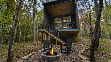 Una cabaña con chimenea de piedra, zona de estar exterior y una escalera que lleva a una terraza.