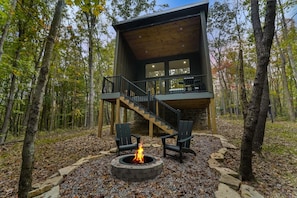 Une cabane dotée d’une cheminée en pierre, d’un espace salon extérieur et d’un escalier menant à une terrasse.