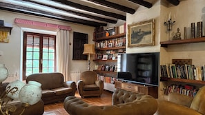 Ein Wohnzimmer mit Kamin, Bücherregalen, Fernseher und einem großen Fenster mit Vorhängen.