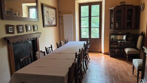 Ein Esszimmer mit einem langen Tisch, Stühlen, einem Kamin, einem Fenster und einem Bücherregal.