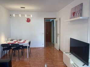 Un comedor con una mesa preparada para cuatro personas, un televisor de pantalla plana y un reloj fijado a la pared.