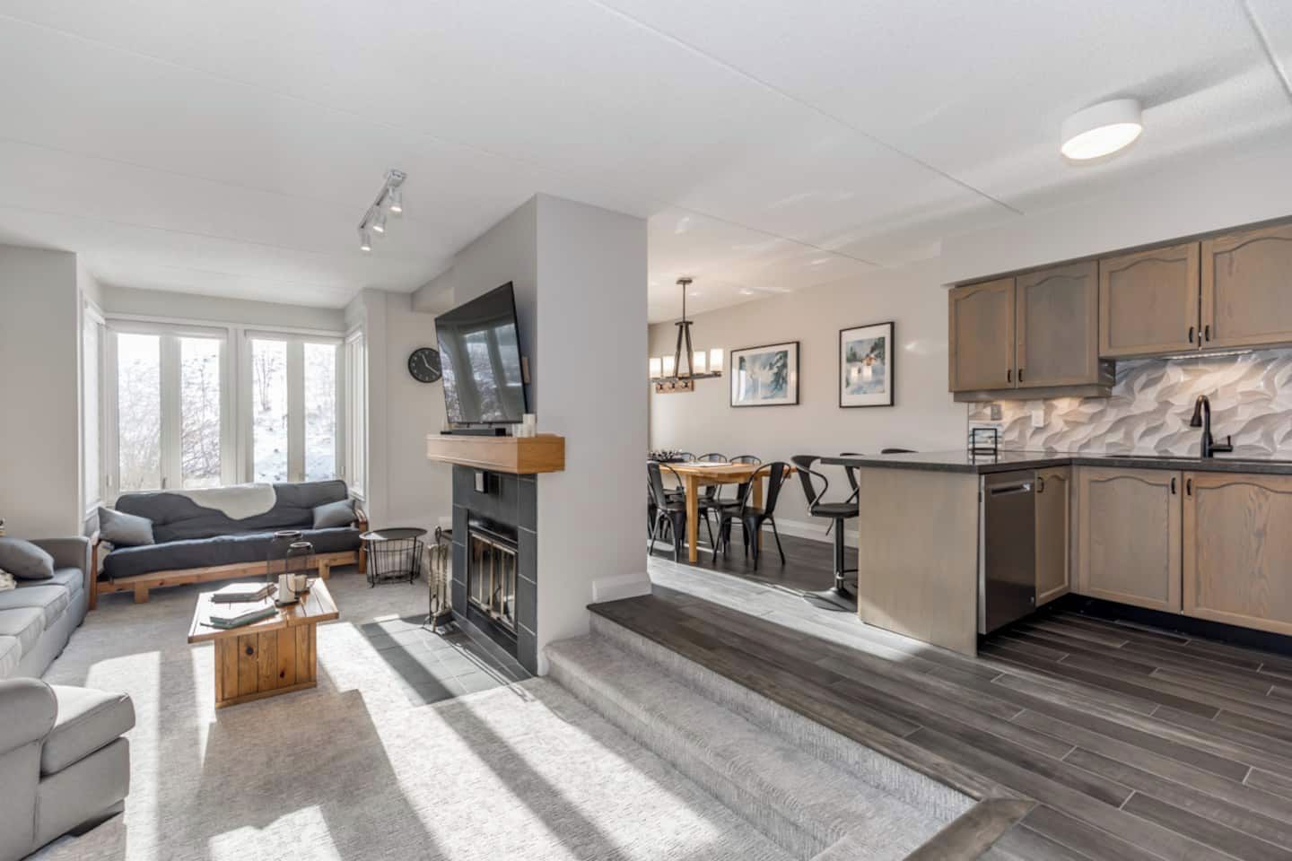 A modern living room with a fireplace, a dining area, and a kitchen with wooden cabinets.
