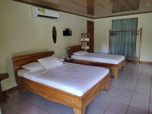 A hotel room with two wooden beds, a wall-mounted air conditioner, a small table with a lamp, and a curtain. - Cecropia Wild Corcovado (Drake Bay)