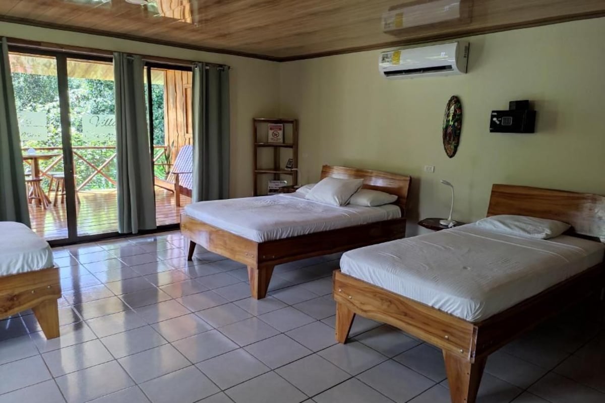 A room with two wooden beds, a tiled floor, an air conditioning unit, and a view through a glass door to an outdoor area.