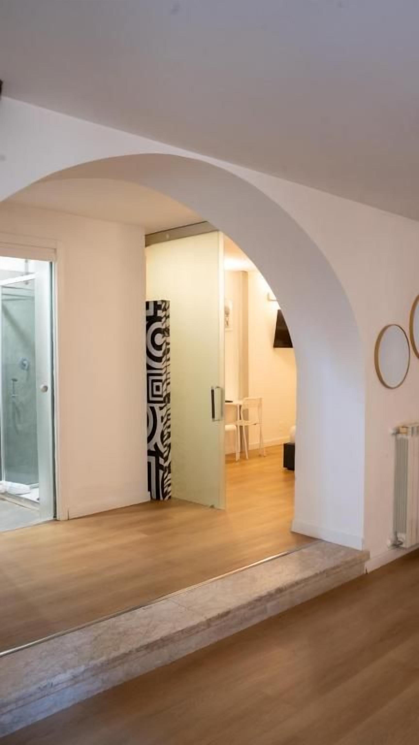 Un pasillo con piso de madera, un arco de entrada y una puerta de vidrio a la izquierda.