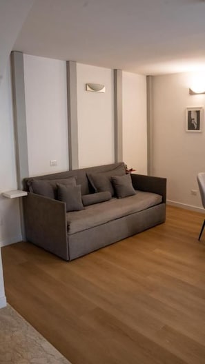 Sala de estar moderna com um sofá cinzento, piso de madeira e luminária fixada na parede.