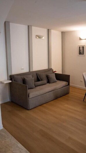 Ein modernes Wohnzimmer mit einem grauen Sofa, Holzboden und einer Wandleuchte.