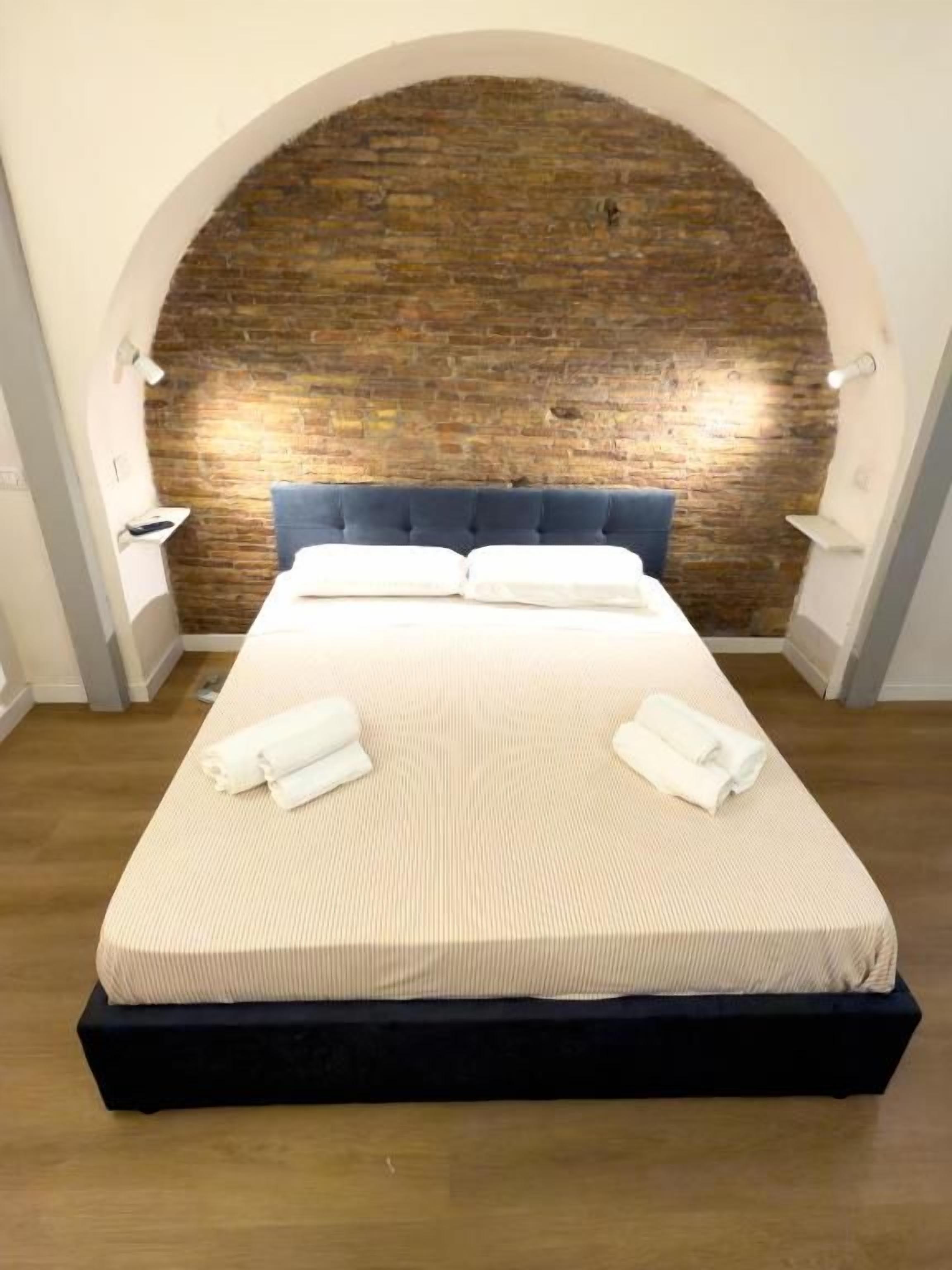 Habitación de hotel con una cama grande, un arco de pared de ladrillo y suelo de madera.