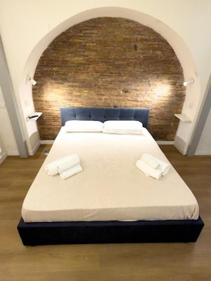 Quarto de hotel com uma cama grande, um arco de parede de tijolos e piso de madeira.