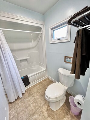 Et badeværelse med badekar, toilet og et vindue.