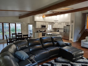 A spacious living room with a large black leather sectional sofa, a dining area with a table and chairs, and a kitchen with white cabinets and stainless steel appliances. - Beautiful 6 Bedroom 3.5 Bath Home with Heated Pool and Jacuzzi and Steam Rooms (Hales Corners)