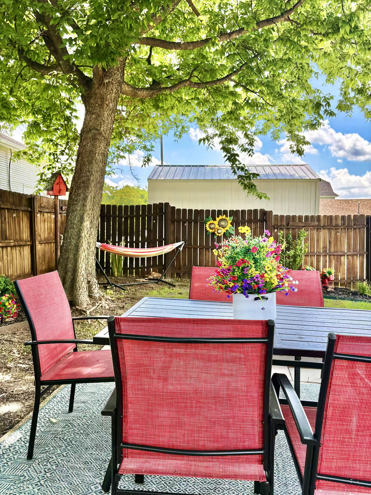 An outdoor patio with a table and chairs, a hammock, and a wooden fence.