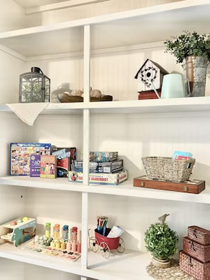 Un estante con varios objetos, incluyendo una casa para pájaros, una planta en maceta y juegos de mesa.