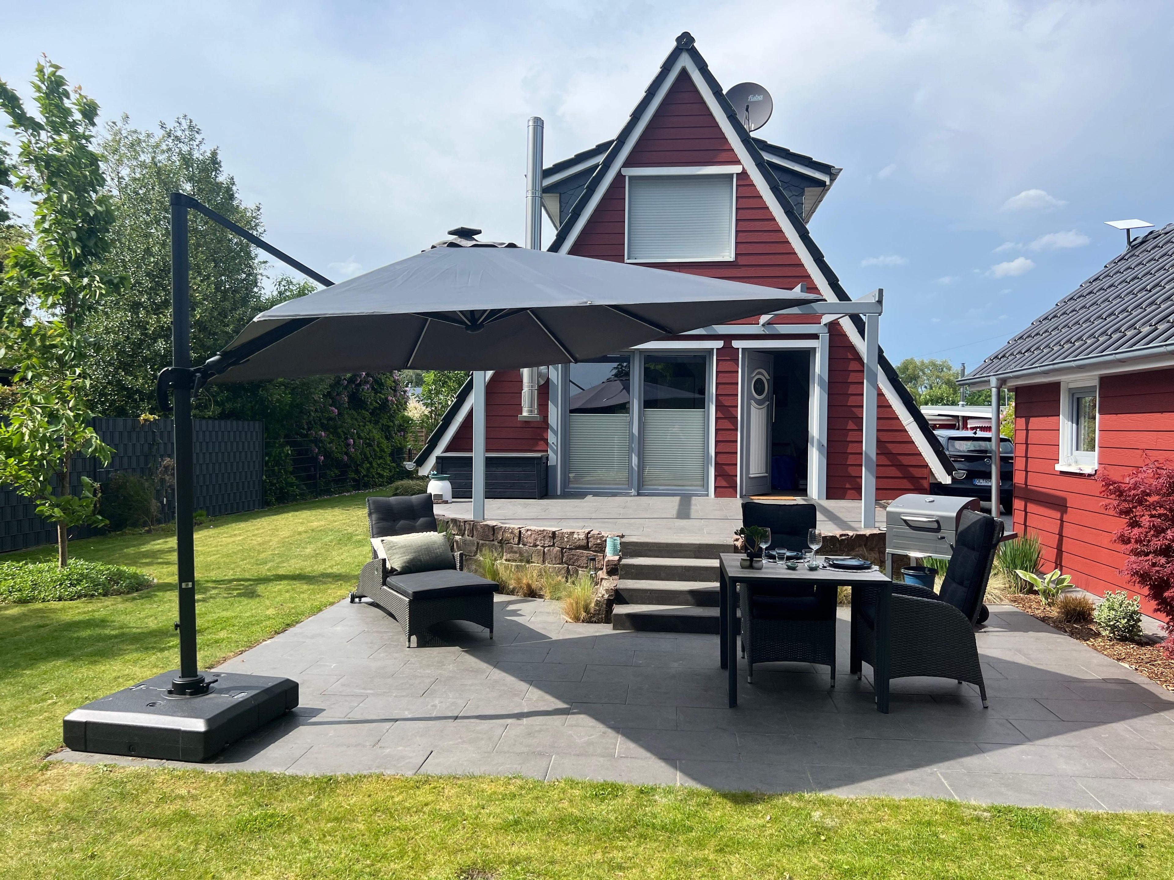 A patio area with outdoor furniture, a grill, and a satellite dish on a house.
