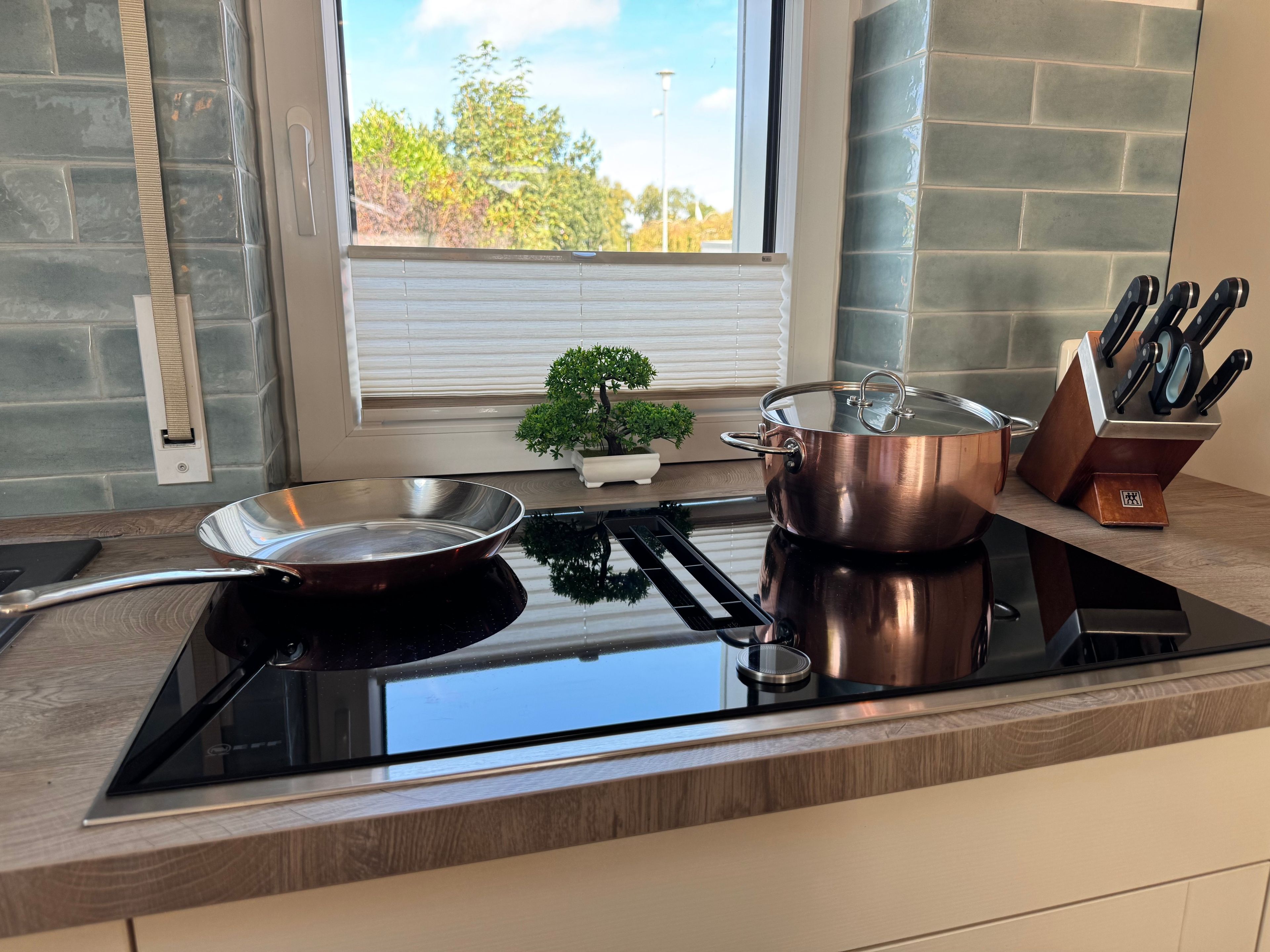 Une cuisine équipée d’une plaque de cuisson à induction noire, d’une casserole en acier inoxydable, d’une marmite en cuivre et d’un bloc à couteaux.
