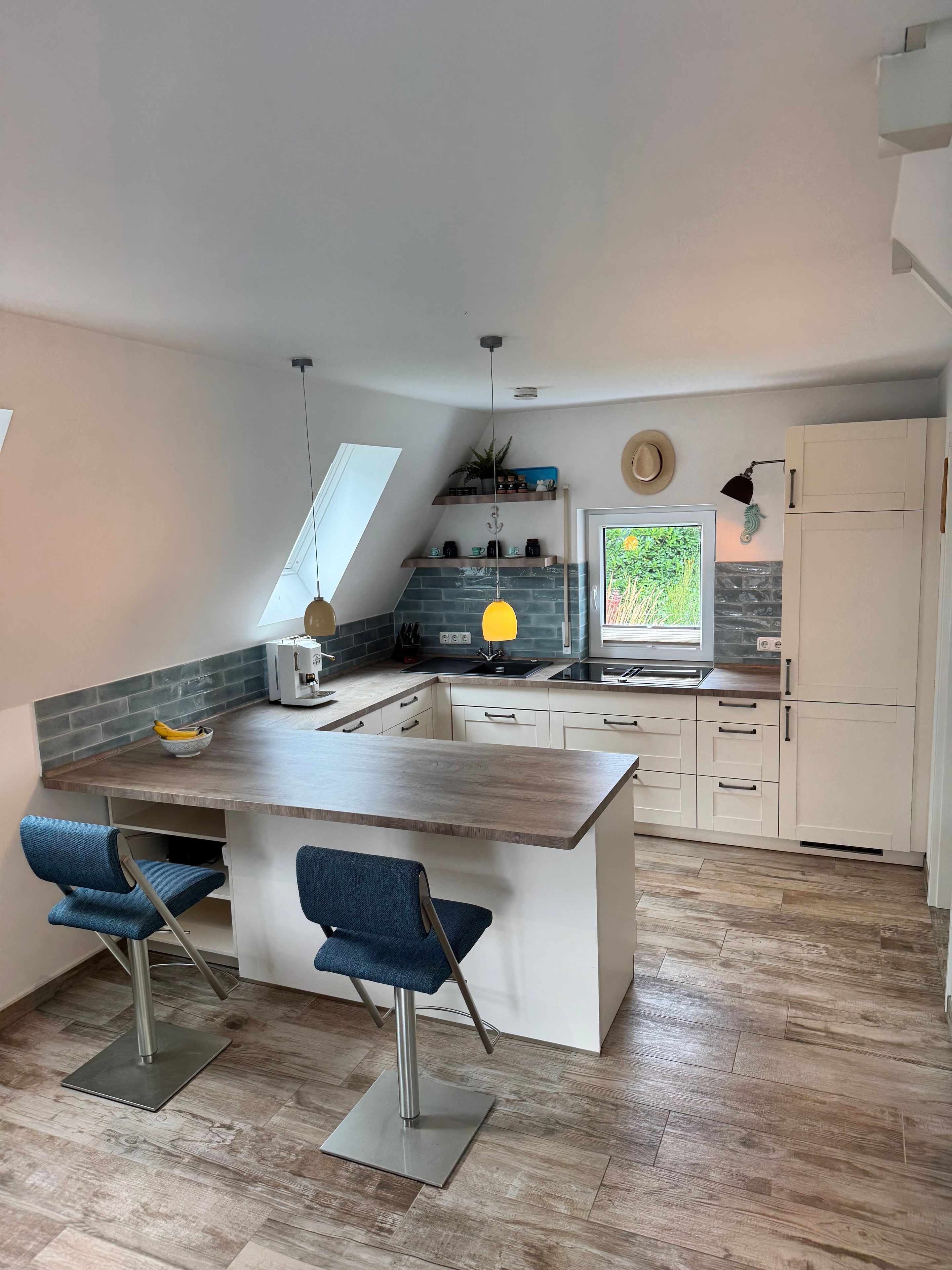 A modern kitchen with a central island, bar stools, a built-in oven, and a large window.