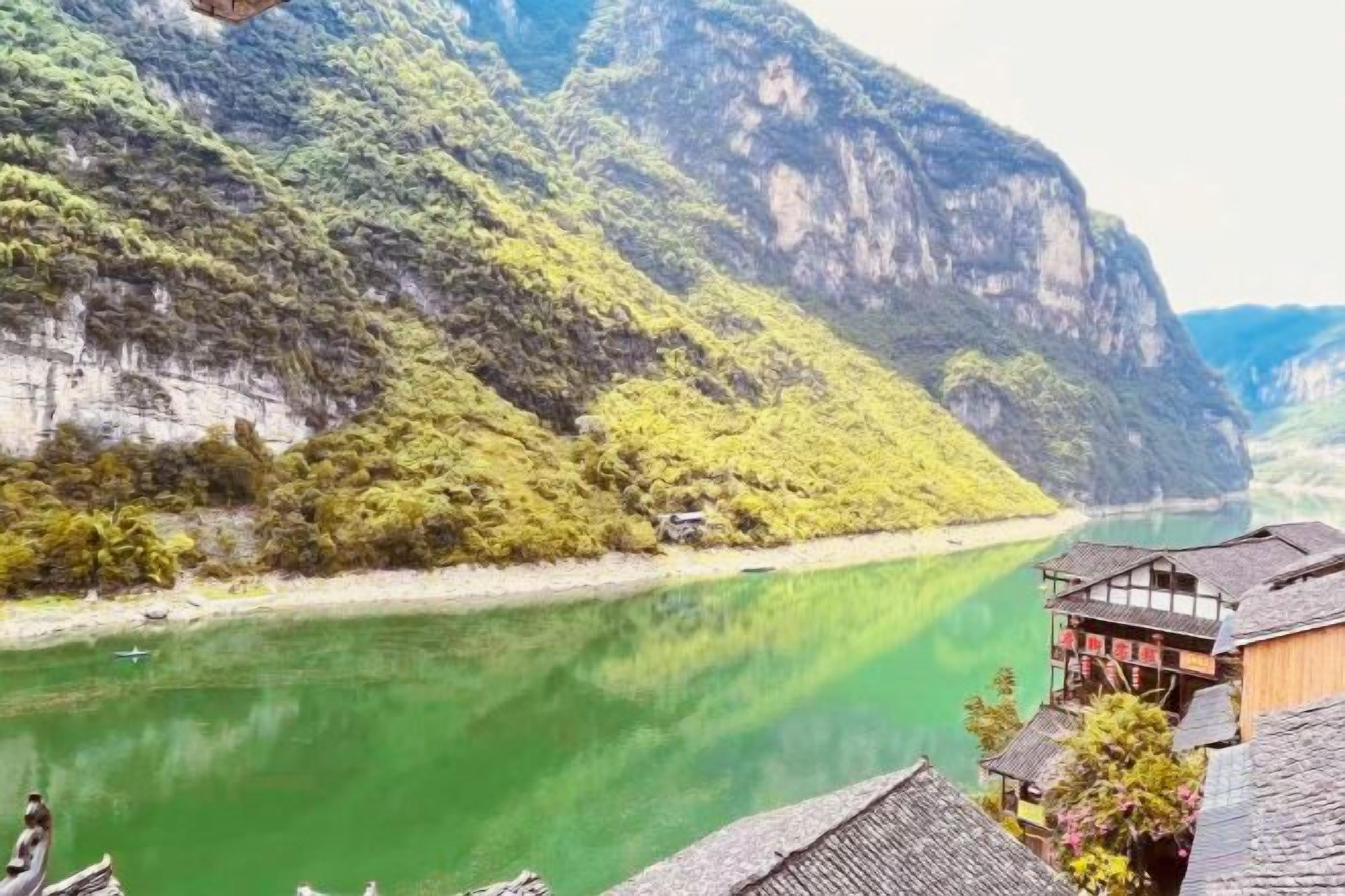 Ein Fluss vor einer Bergkulisse, traditionelle Gebäude mit geneigten Dächern und einem klaren Himmel.