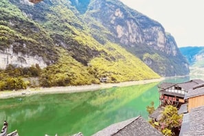 Un río con montañas al fondo, edificios tradicionales con tejados inclinados, y un cielo despejado.