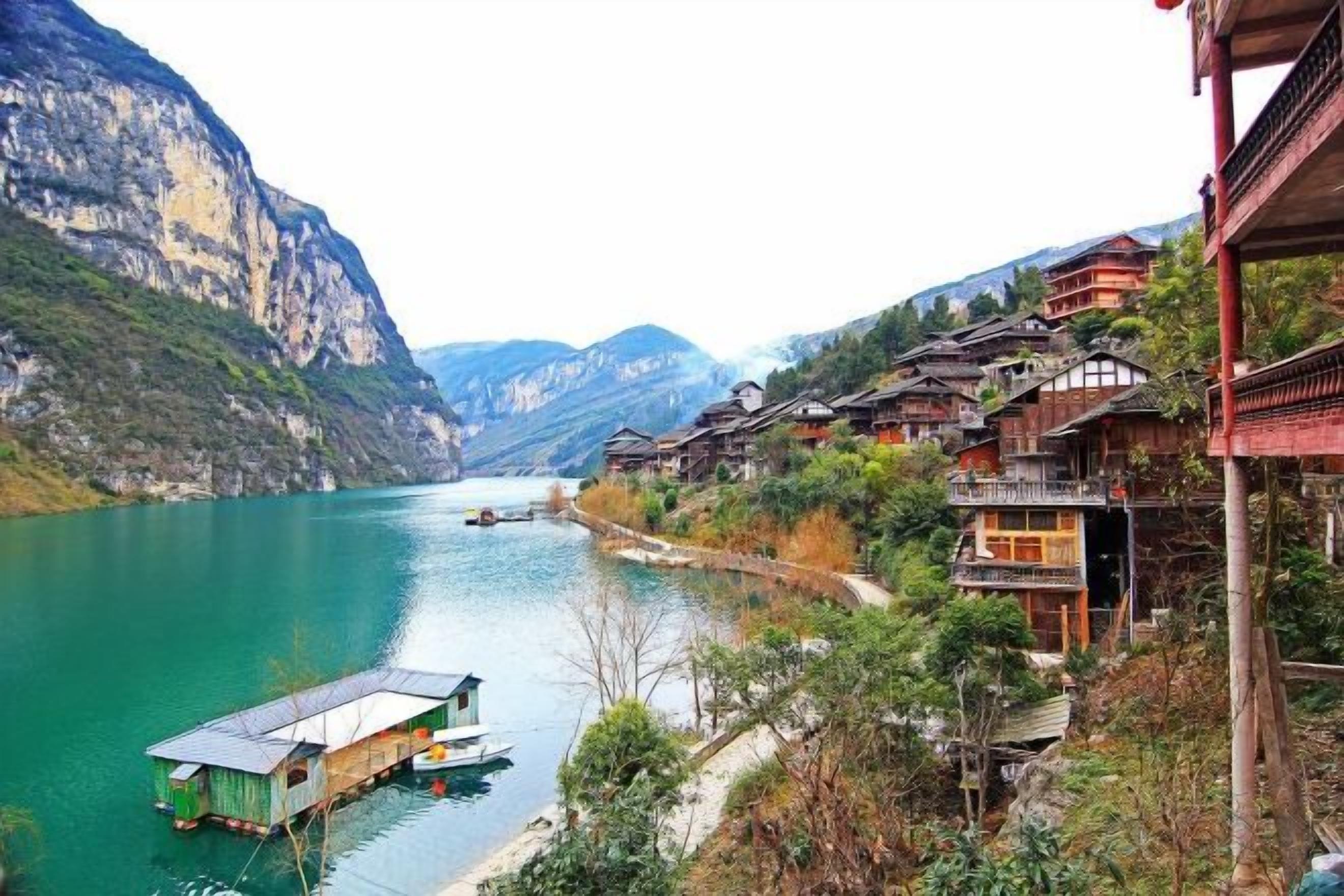A traditional wooden building with a balcony, a river, and mountains in the background.