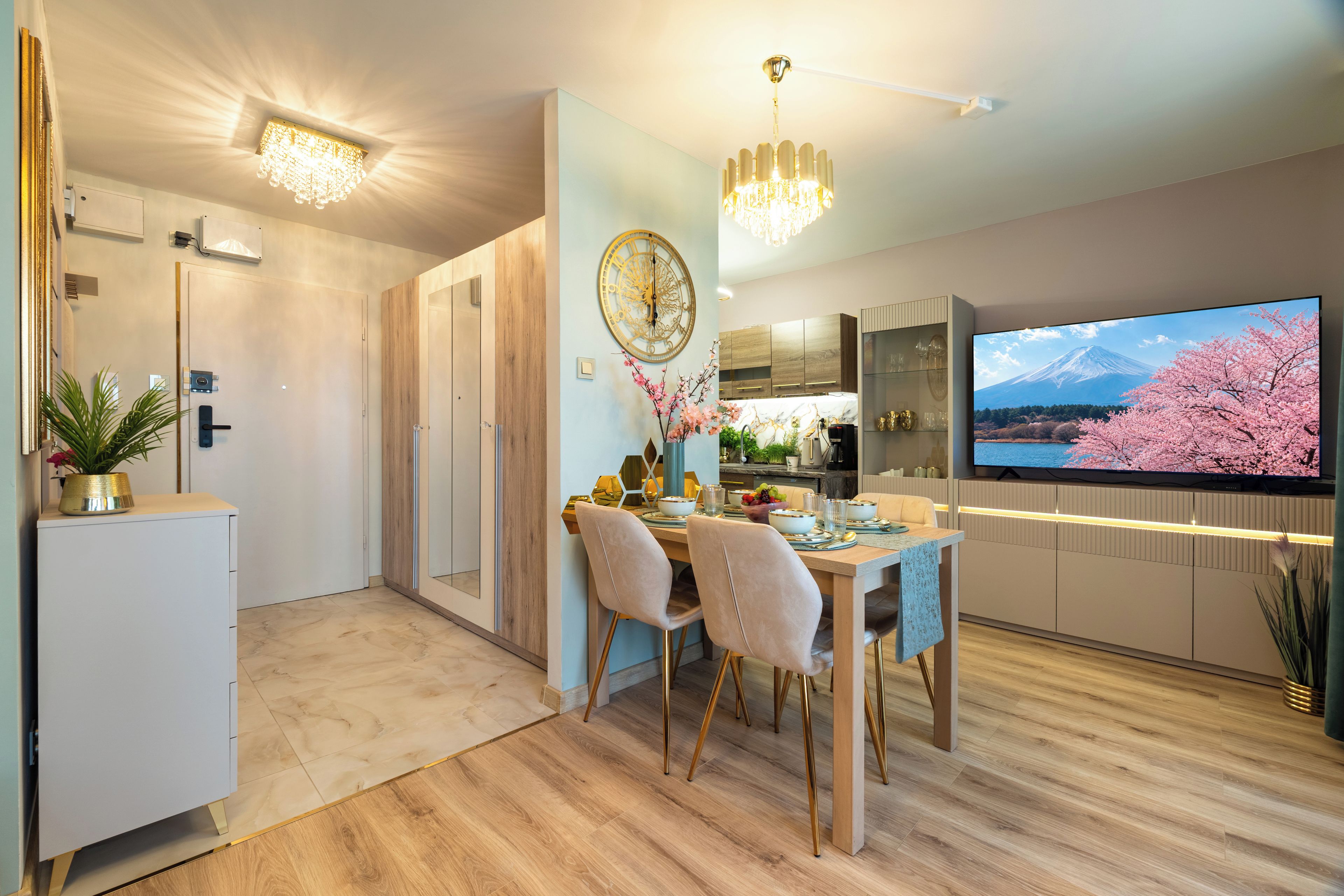A modern dining area with a wooden table, chairs, and a television displaying a scenic view.
