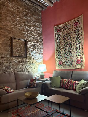 Una sala de estar acogedora con una pared de piedra, un sofá, una mesa de centro y un tapiz estampado.