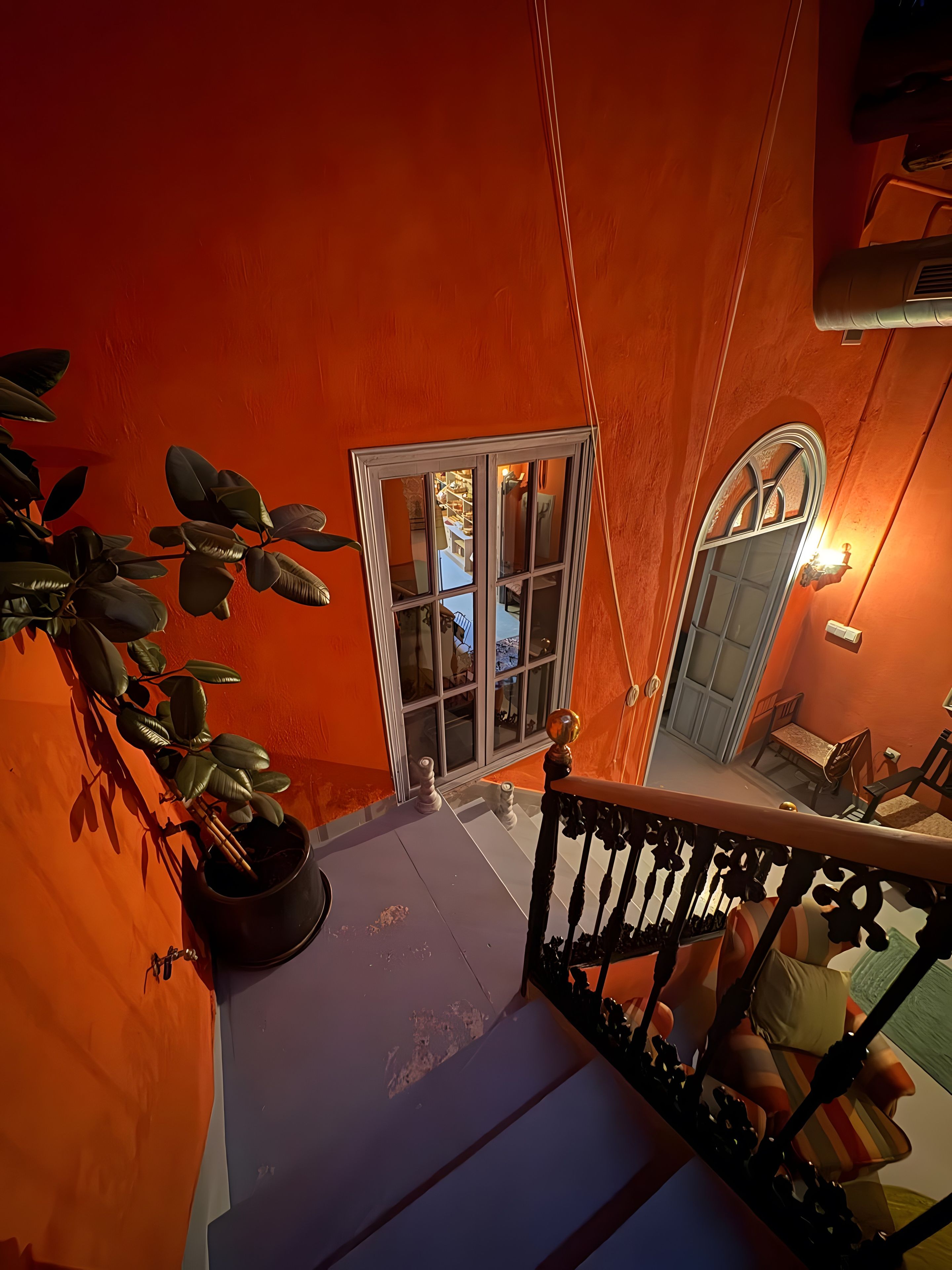 A staircase leading to a room with a view of a balcony, a potted plant, and a door with glass panels.