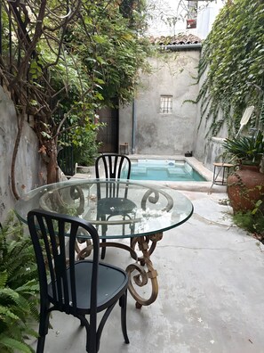 Una mesa con cubierta de vidrio y sillas en un patio con piscina.