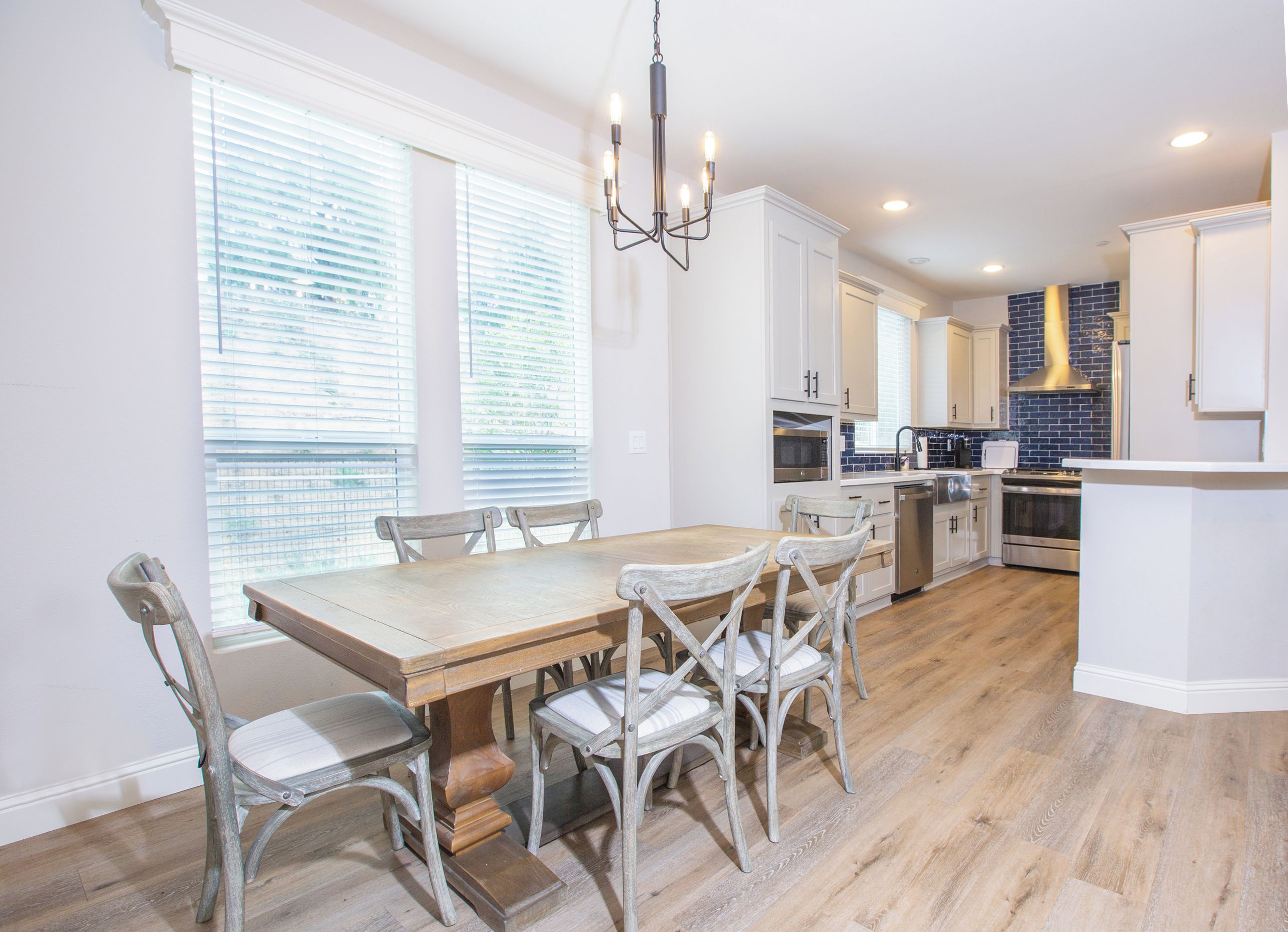 A modern kitchen with white cabinetry, a wooden dining table, and a built-in oven.
