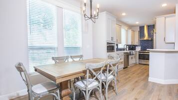 A modern kitchen with white cabinetry, a wooden dining table, and a built-in oven.