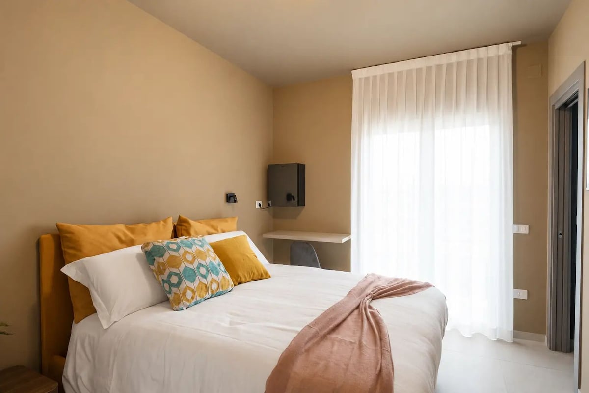 Habitació d'hotel amb llit, escriptori i finestra amb cortines.
