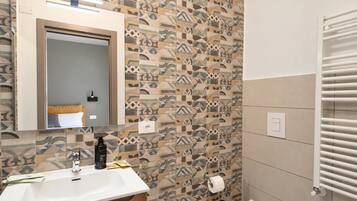 Une salle de bain avec un mur recouvert de carreaux décoratifs, un miroir au-dessus du lavabo, un distributeur de serviettes et des toilettes avec un porte-serviettes.