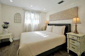 A hotel room with a large bed, bedside tables, a window with curtains, and a wall-mounted artwork. - New Listing (Kissimmee)
