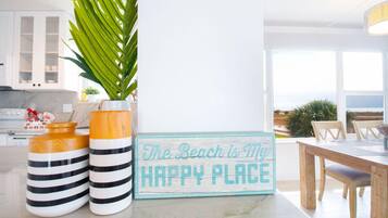 A kitchen with white cabinets, a potted plant, two striped vases, and a sign that reads 'The Beach is My Happy Place.'