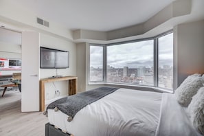 A modern bedroom with a large bed, a television, and a city view. - 2BR High-Rise • City View (Toronto)