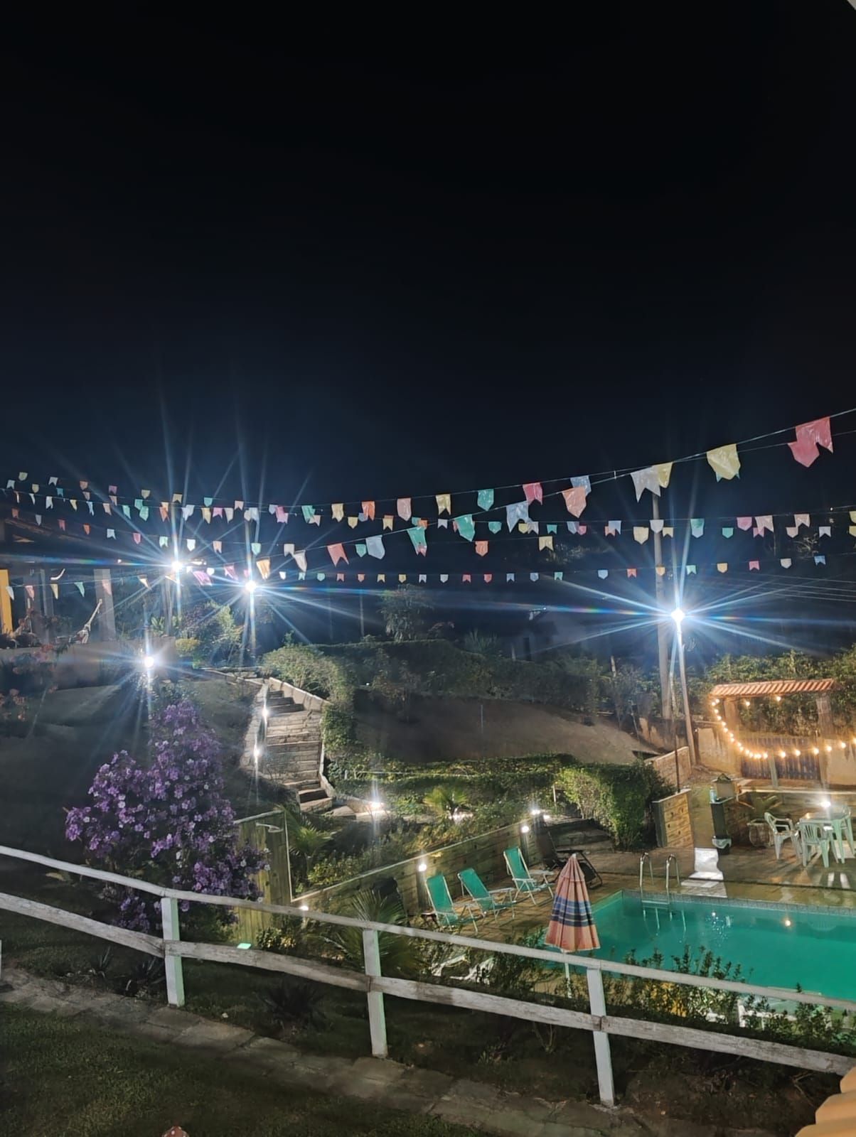 A nighttime view of a pool area with string lights and a white fence.