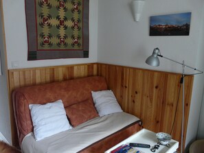 A bedroom with a wooden headboard, a bed with two pillows, a bedside table with a lamp, a remote control, and a small tray with a bowl. - New Listing (luz saint sauveur)