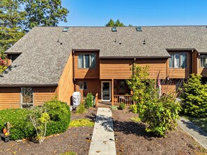 Une maison en bois à deux étages, dotée d’un porche couvert et d’un petit jardin.