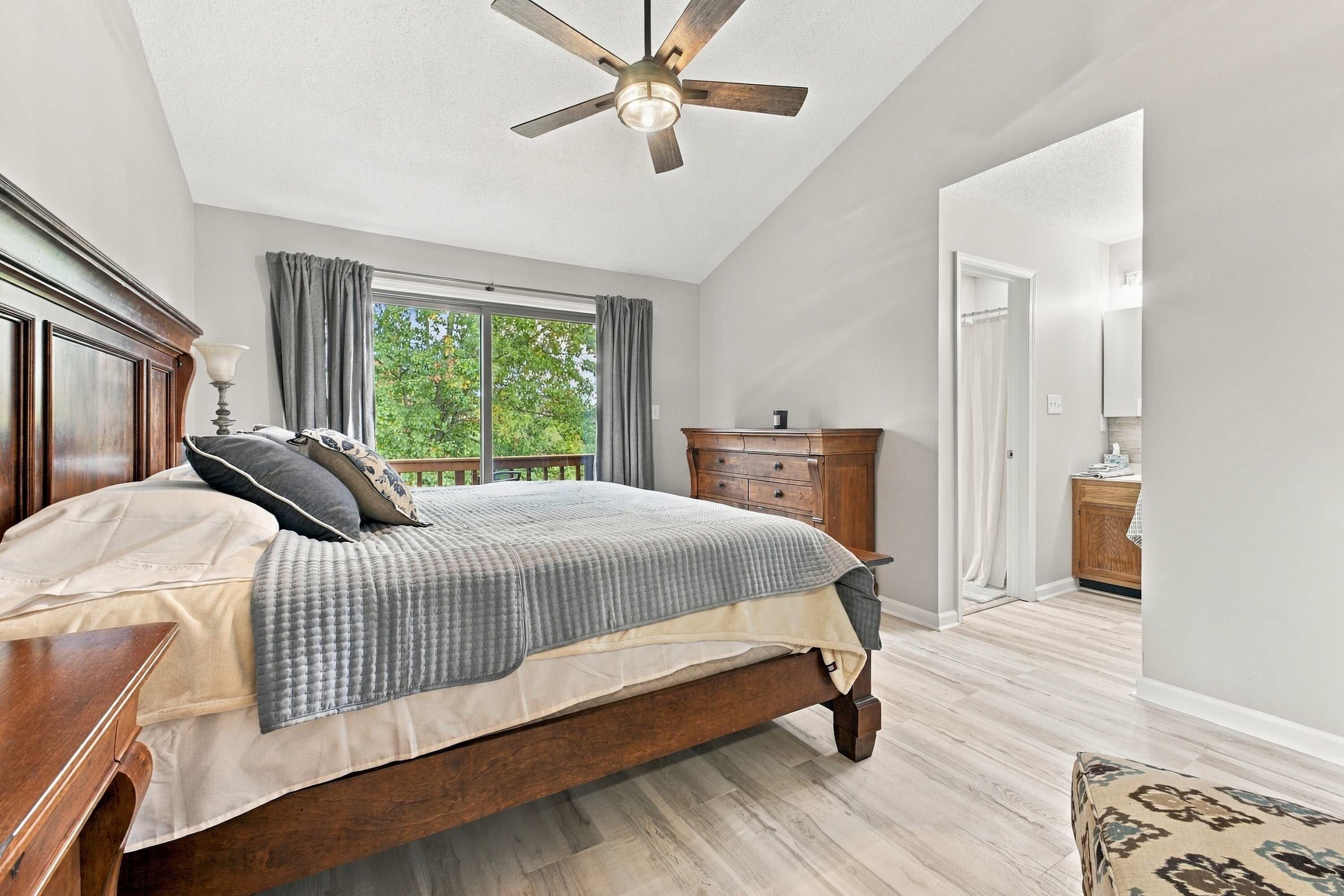 A bedroom with a wooden bed, a ceiling fan, a window with curtains, and a wooden dresser.