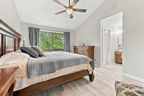 A bedroom with a wooden bed, a ceiling fan, a window with curtains, and a wooden dresser.