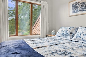 Ein Schlafzimmer mit einem Bett, einem Nachttisch, einem Fenster mit Vorhängen und einem Bild an der Wand.