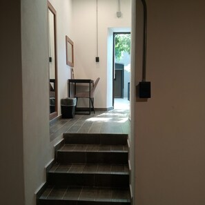 A staircase leading to a room with a chair and a table, a trash bin, and a door leading outside.