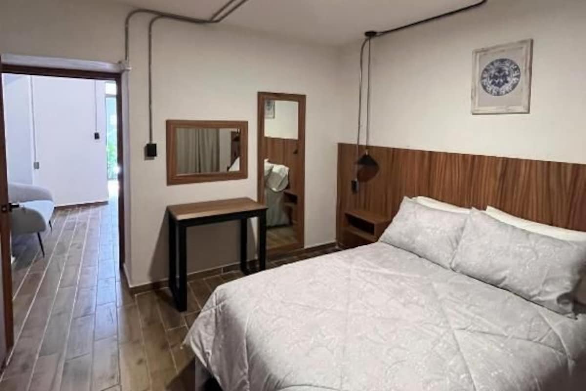 Quarto de hotel com cama, mesa de cabeceira, espelho e quadro pendurado na parede.